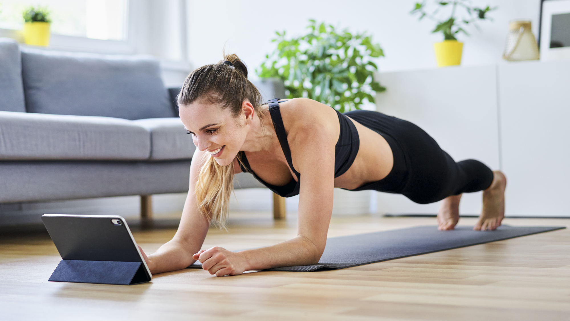 Woman in plank pose looking at a tablet computer in a living room