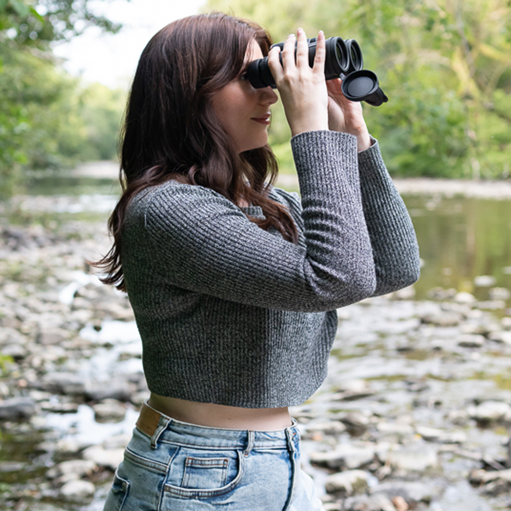 article author Kimberley Lane using a pair of binoculars next to a stream