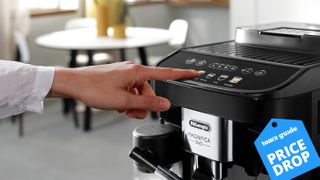 A finger pressing a button on the De&#039;Longhi Magnifica Evo with a Tom&#039;s Guide Price Drop deals label