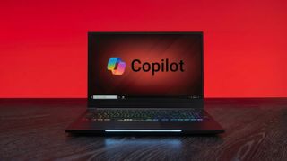 A laptop with a colorful backlit keyboard is open on a dark wooden table. The screen displays the "Copilot" logo on a red gradient background.