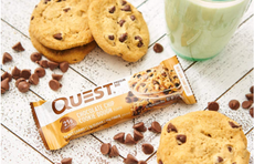 A quest protein bar is surrounded by cookies and milk on a countertop.
