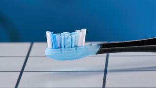 a black electric toothbrush with a small touchscreen and a blue toothbrush head and a square charging stand