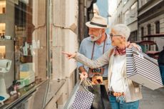 A senior couple window shopping while carrying bags.