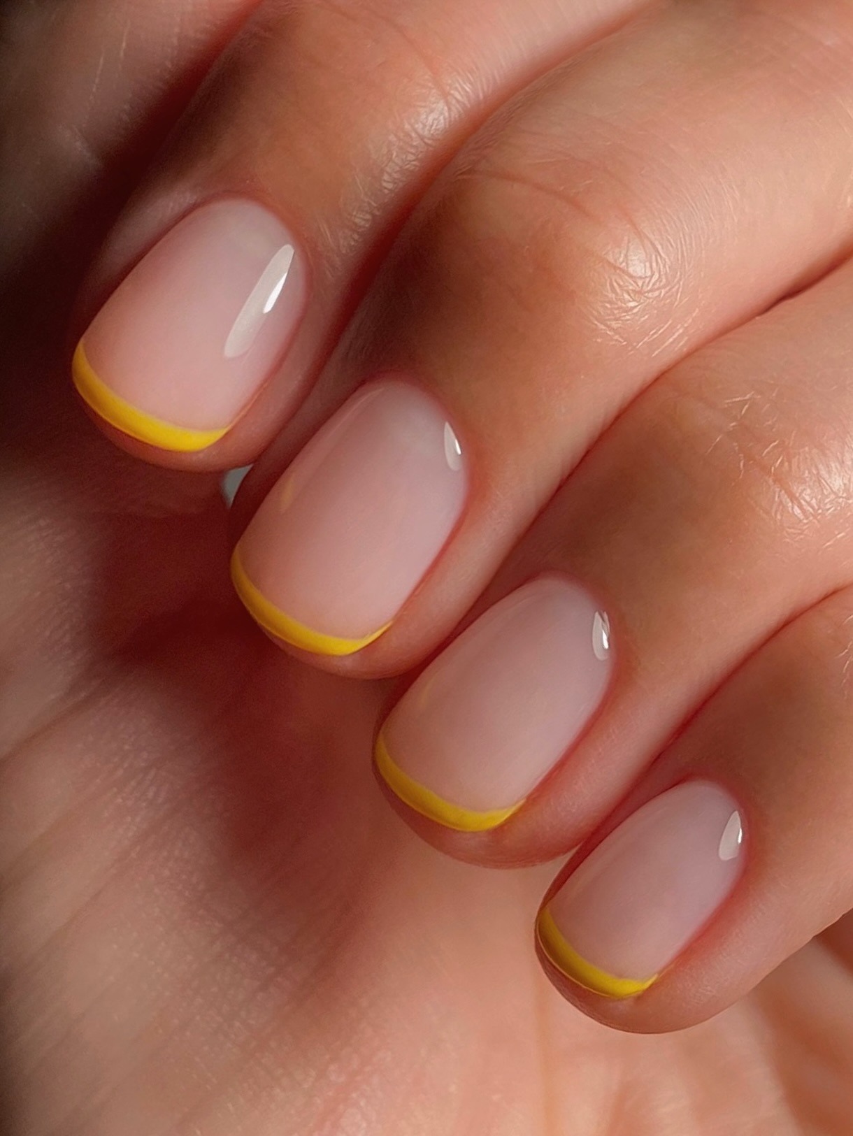 A close-up of a bright yellow French manicure on short nails