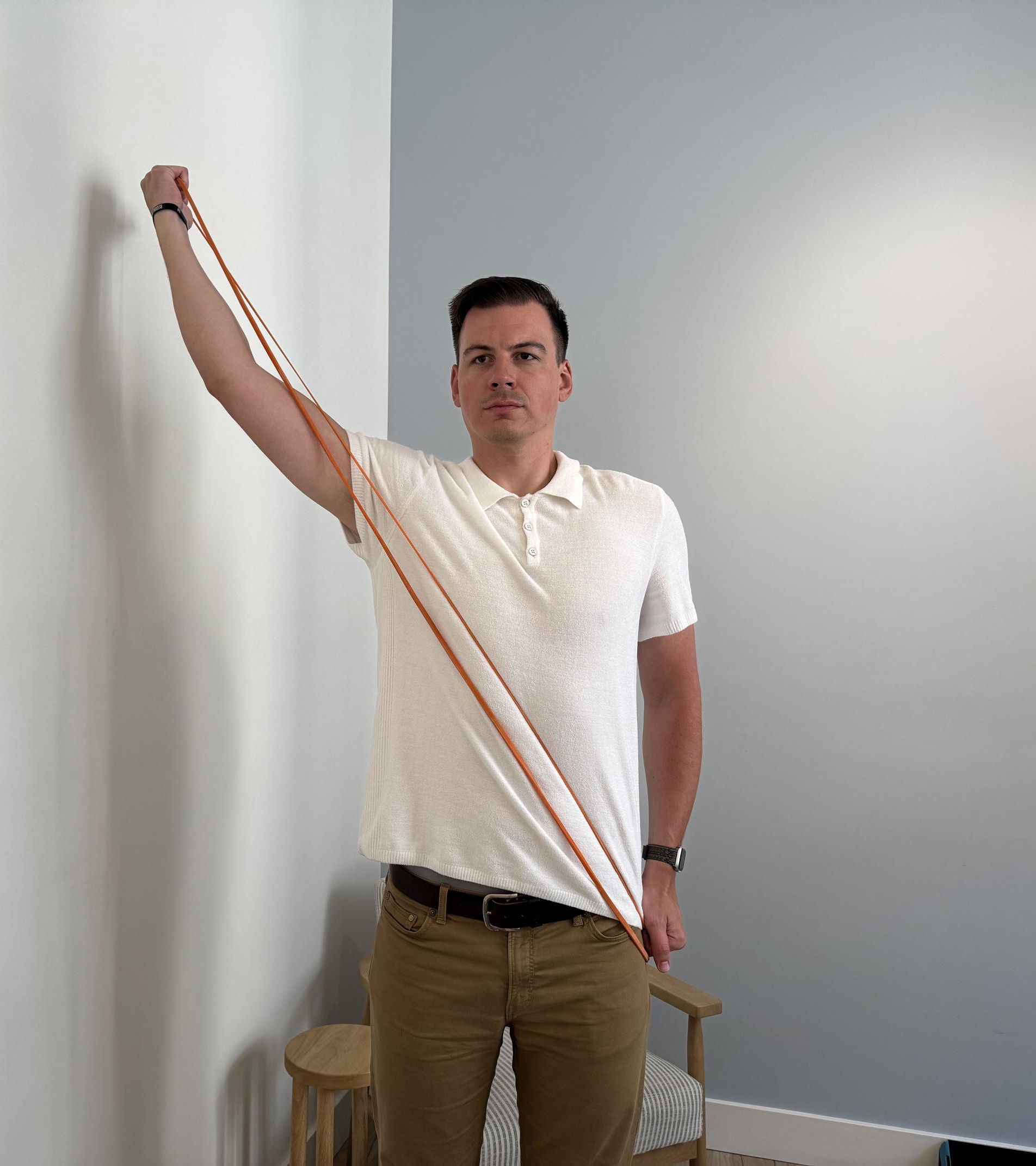 A man holding a thin orange resistance band with one hand by his left hip and the other above his right shoulder