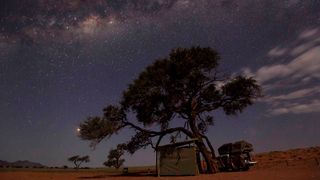 a tent under a tree with a star filled sky above.