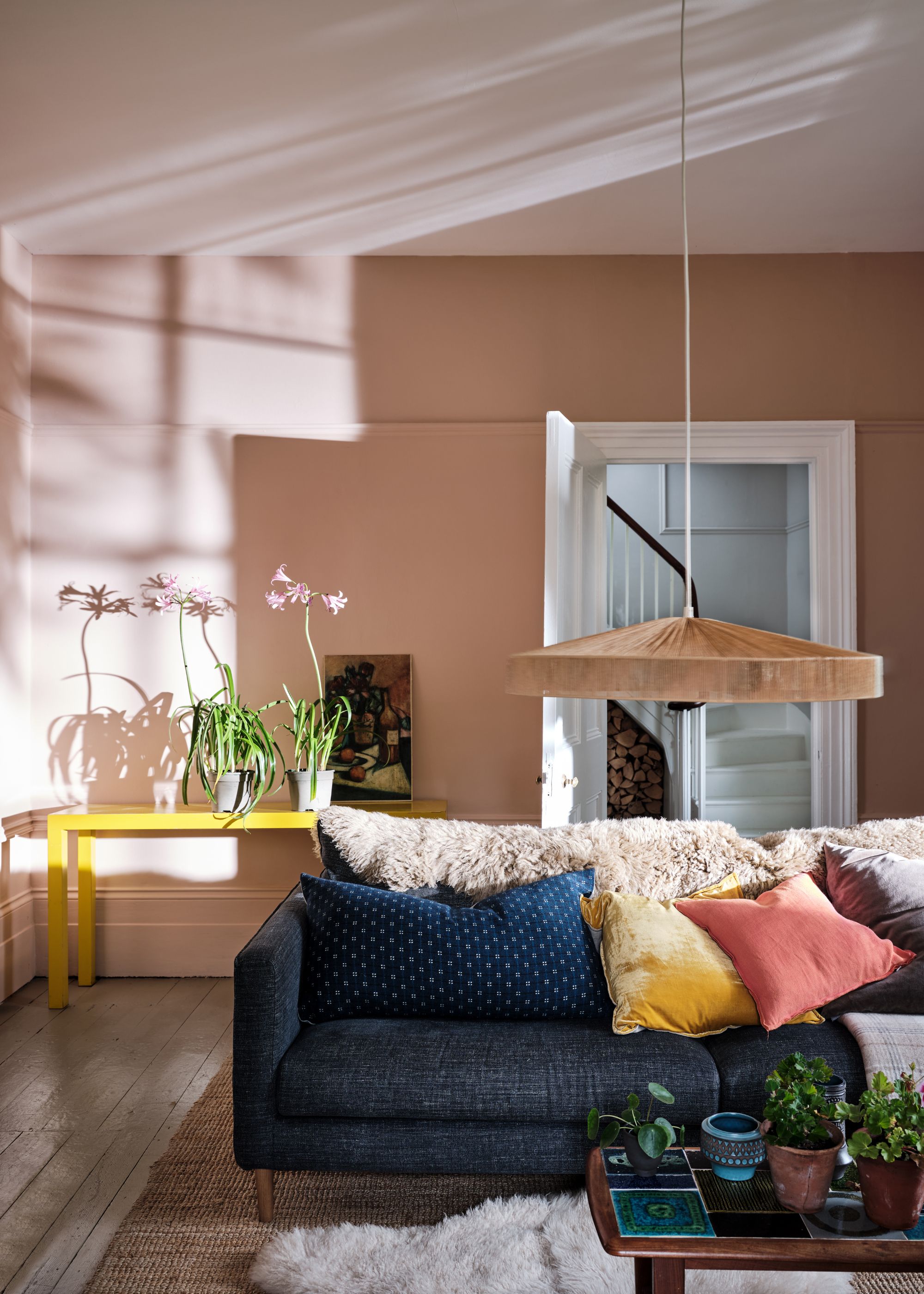A living room with pink walls and a navy sofa with colorful cushions and a yellow table in the corner.