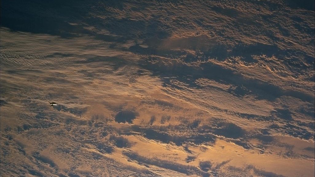 images captured from space show earth covered in clouds below and a small black object visible towards the left of the image.