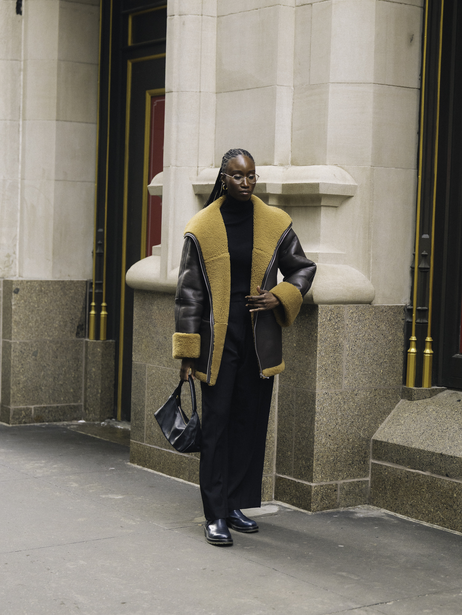 woman wearing fur-trimmed coat, black top, black pants, shoes, and a shoulder bag