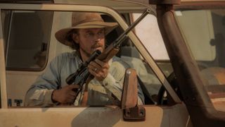 Graham Lawson holding a gun as he stands behind a car door in Territory.