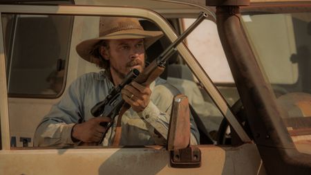 Graham Lawson holding a gun as he stands behind a car door in Territory.