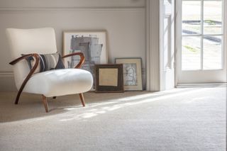 A white mid-century armchair on a white carpet with various framed pictures leaning against the wall behind it