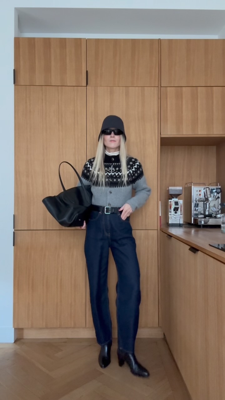 Woman wears a fair isle cardigan, white turtleneck, high waisted jeans, wool bucket hat and black ankle boots.