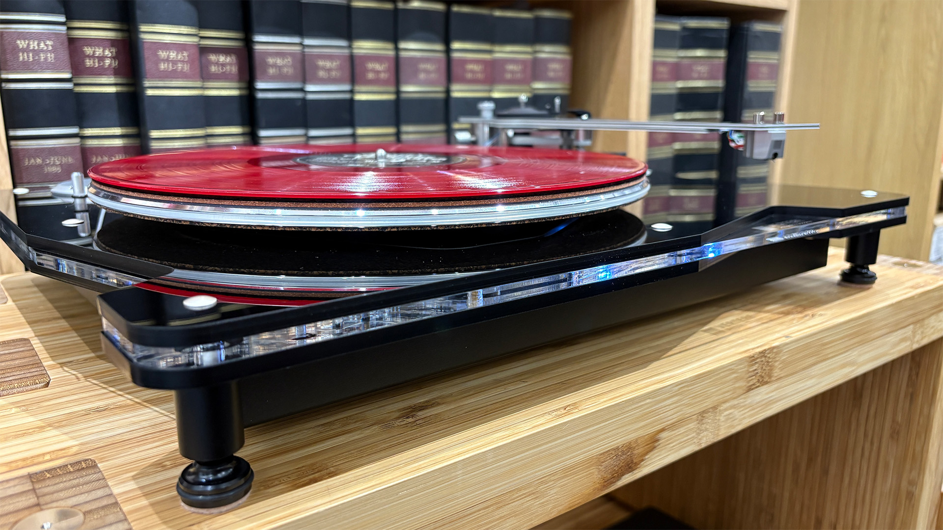 Vertere DG-X turntable on wooden hi-fi rack in front of bookcase level view with pink vinyl record on platter