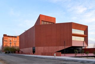 Daytime image of the new contemporary Art Centre, red exterior, road, surrounding trees, another red brick building in the distance, blue cloudy sky