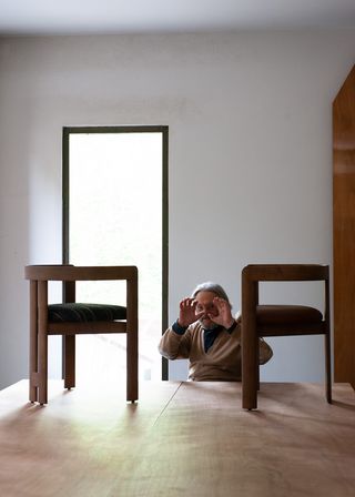 Tobia Scarpa sitting at a table on which are displayed two models of his Pigreco chair upholstered in textile and leather