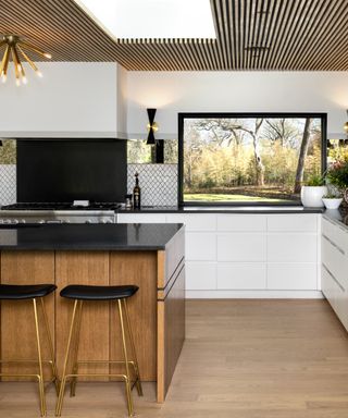 Wood and white kitchen with wood kitchen island and paneled ceiling, white units, black countertop, view of outside, pendant light, cooker hood