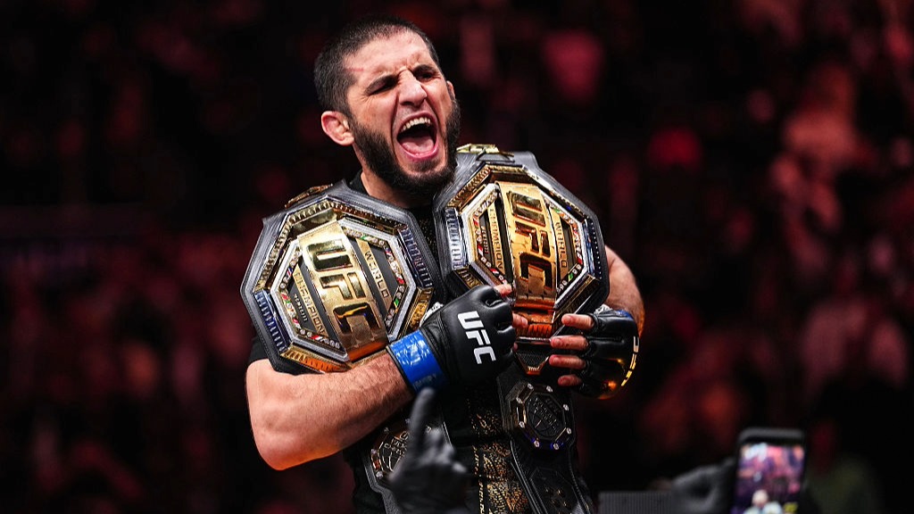 Islam Makhachev celebrates winning the UFC Welterweight Championship by posing with two belts over his shoulders.