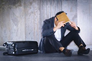 Stressed businessman sitting on ground with suitcase.