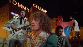 John Entwistle and Pete Townshend playing behind Roger Daltry while Elton John watches in The Who's Tommy.