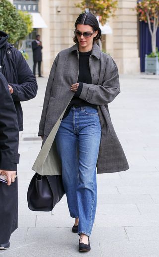 Kendall Jenner in Paris wearing a gray car coat, black sweater, jeans, and black ballet pumps in March 2025.