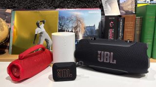An assortment of differently-sized Bluetooth speakers on a white desktop in front of some vinyl records