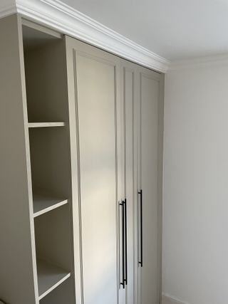 An IKEA PAX wardrobe from a side angle painted a light grey with added trim and integrated shelving