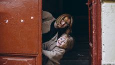 A mother and young son peek playfully from behind a large, red door.
