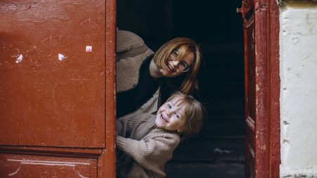 A mother and young son peek playfully from behind a large, red door.