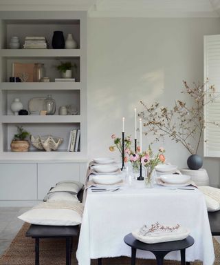 laid dining table with bowls and vases of flowers with open shelving on the wall