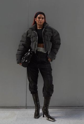 a roundup of the best puffer jackets shown in a photo of a woman wearing a gray puffer coat over a black cropped tank top with black cargo pants tucked into black ankle boots