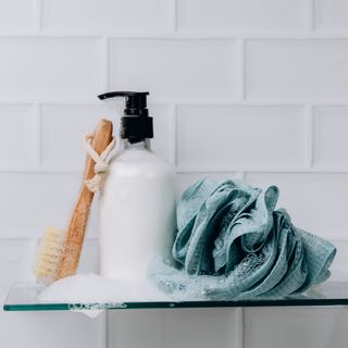 closeup of shower products bodywash brush and lufa on white subway tile