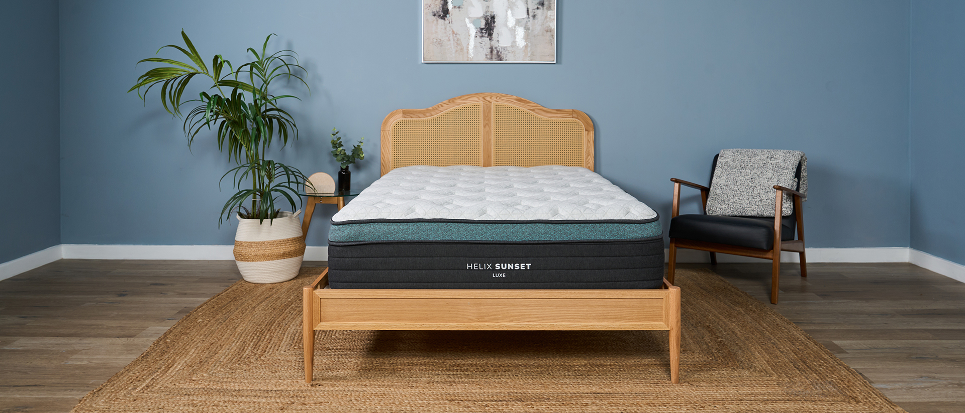 The image shows the Helix Sunset Luxe Mattress on a wooden frame against a blue bedroom wall