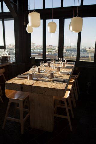 Wooden set table with cream lights hanging from the ceiling next to a window with a view of the harbour