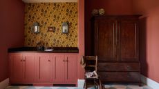 A laundry room with pink walls and cabinets and a yellow floral wallpaper feature wall