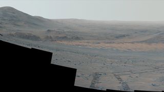 looking down the slope of a crater rim on mars, with rover tracks in the foreground