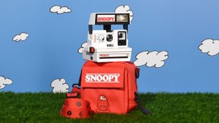 Retrospekt Snoopy polaroid camera and bag on grass with cartoon clouds on blue sky background