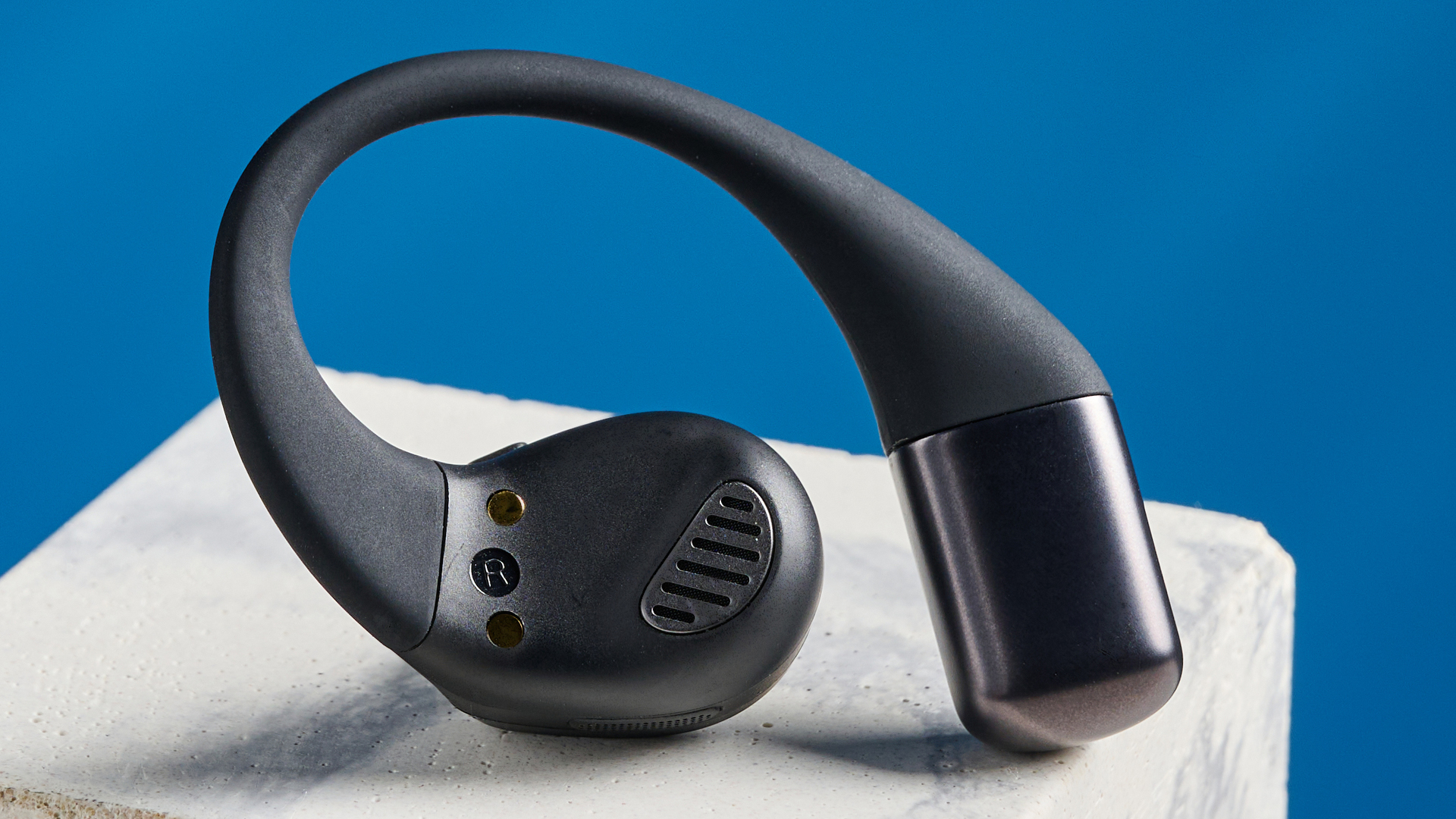 Jlab epic open sport open-earbuds in a black colorway photographed on a blue background.
