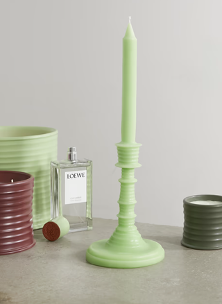 tall green candlestick with a loewe home fragrance and other accessories around