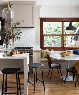 Kitchen with dark wooden window frames, wooden flooring, marble round dining table, bench seating, kitchen island
