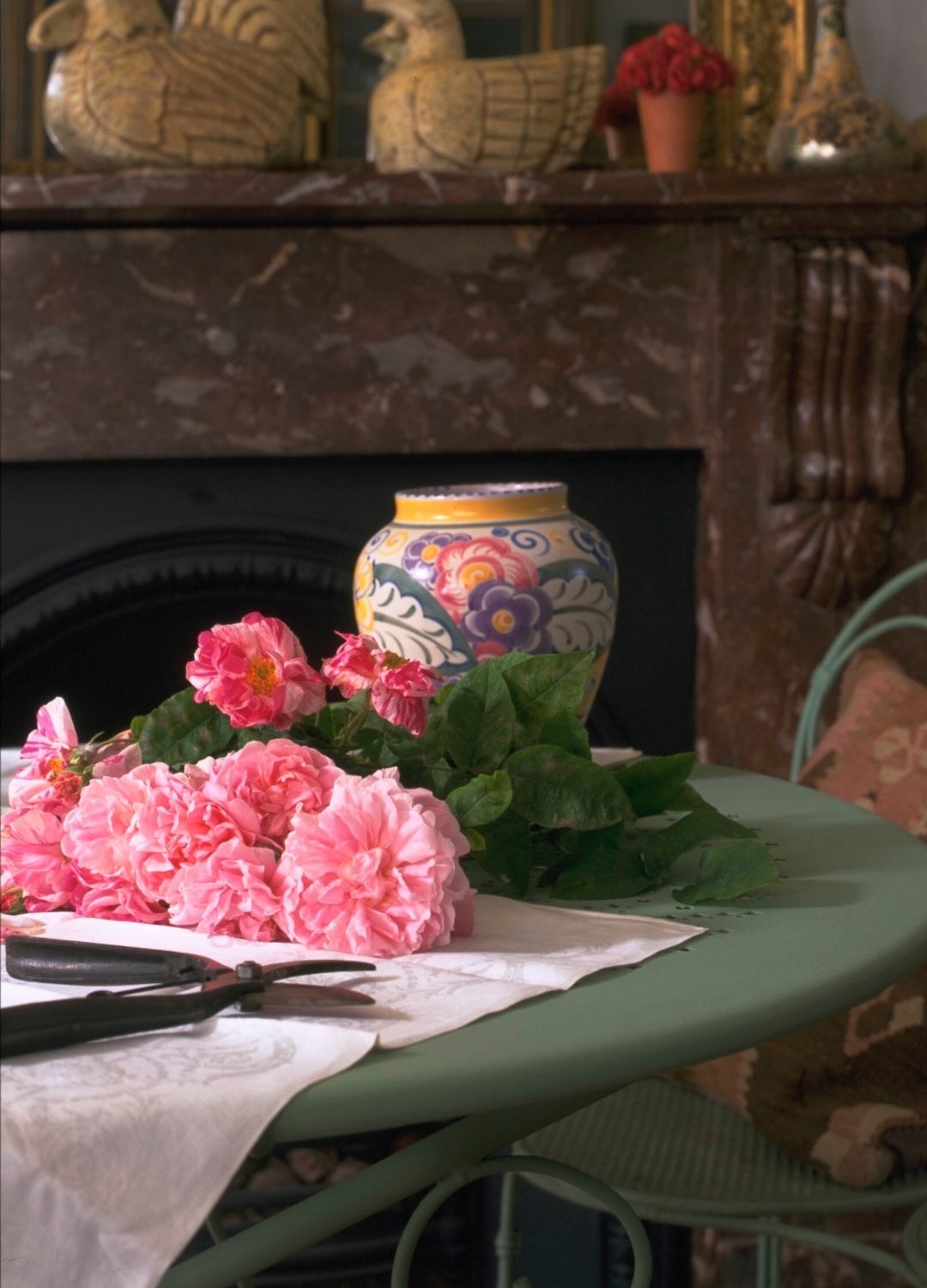 picture of cut roses next to a ceramic vase and secateurs on green table