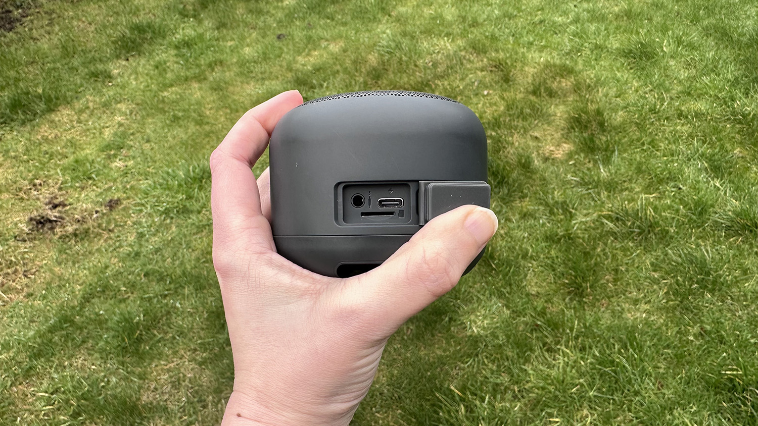 Someone holding the Nokia Portable Wireless Speaker 2 over grass and showing the ports on the rear of the speaker.