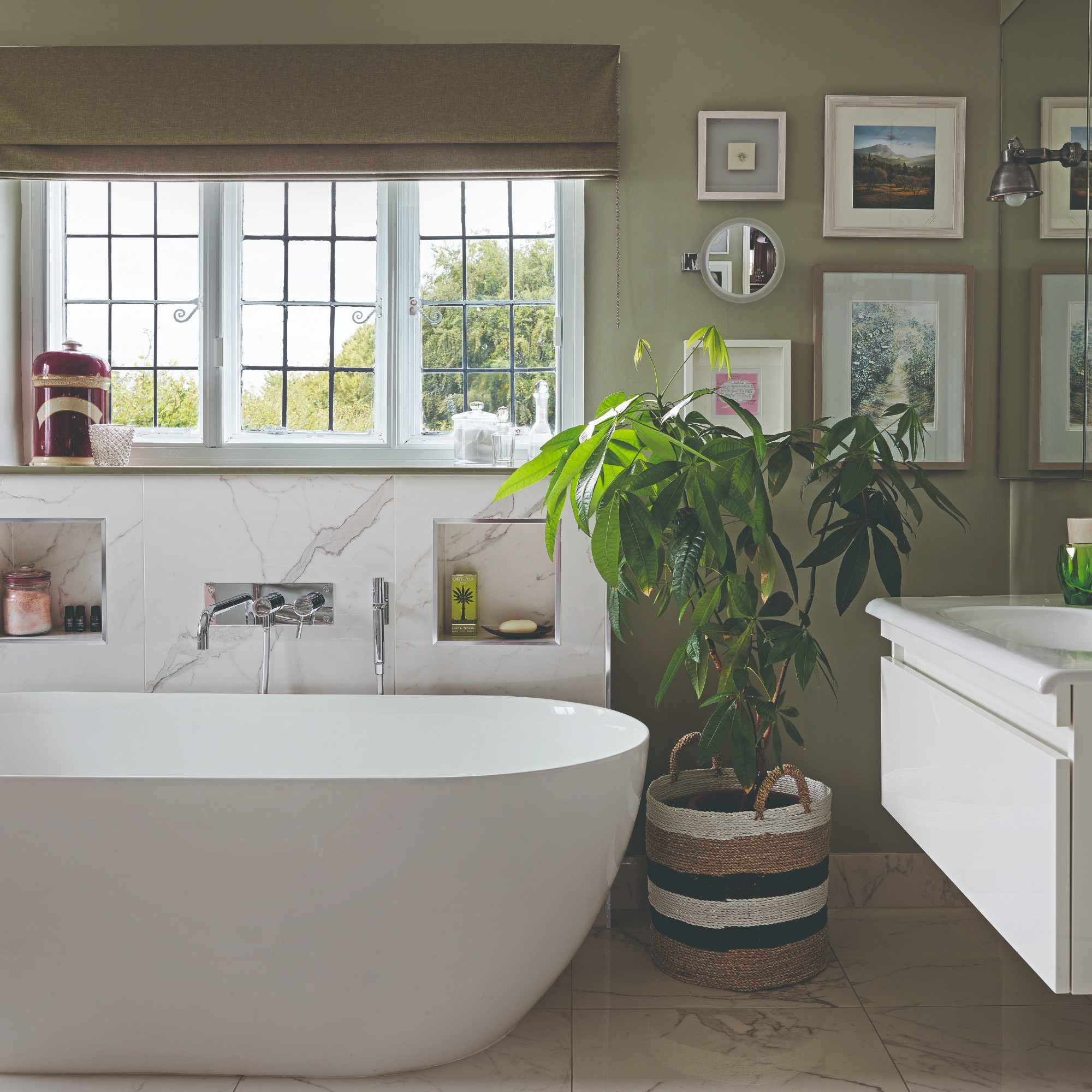 A sage green-painted bathroom with a bathtub and a gallery wall by the sink
