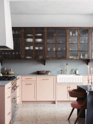 White kitchen with light peach painted cabinetry and floating wooden cabinets that have textured glass doors