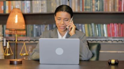 A lawyer talks on the phone at her desk with her laptop open.