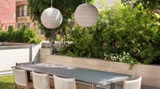 an outdoor dining space with pendant above and a planter behind the table