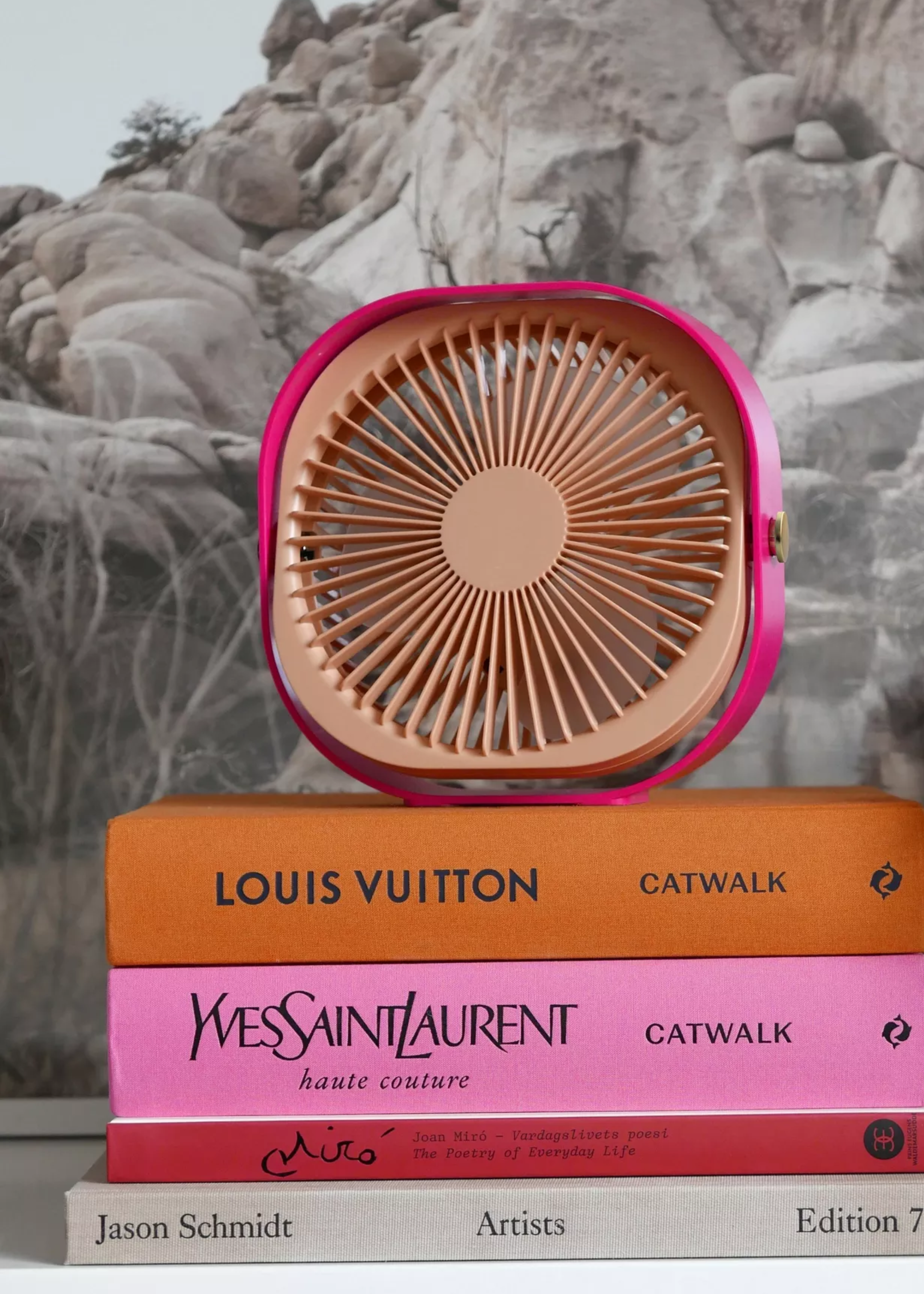 A pink and peach table fan on a stack of coffee table books