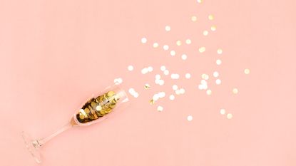 champagne glass full of gold confetti spilling onto pink background