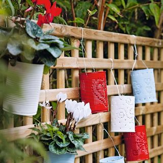 An array of red and white painted tin cans containing various plants suspended from a trellis.