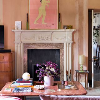 Dusty pink and purple painted wall with marble coffee table decorated with books and trays, fireplace displaying artwork